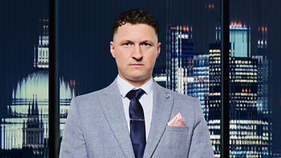 A man in a grey suit (Levi Hague) stands in front of a city landscape at night 