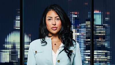 A woman in a blue jacket (Pascha Myhill) and tousled hair poses outside a city landscape in the dark 