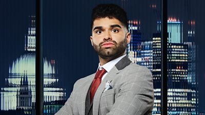 A man in a grey suit (Priyesh Bathia) poses outside a city landscape at night 