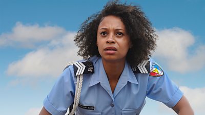 Close-up photo of Catherine Garton in character as Sergeant Mattie Fletcher. Wearing a blue police uniform with badges for Sant Marie. 