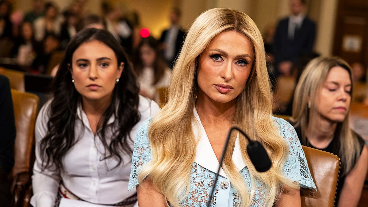 Paris Hilton looking serious wearing a seagreen dress in front of a podium.