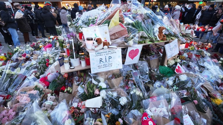 People stand around floral tributes and candles placed outside the sealed off Le Constellation bar in Crans-Montana, Swiss Alps, Switzerland.
