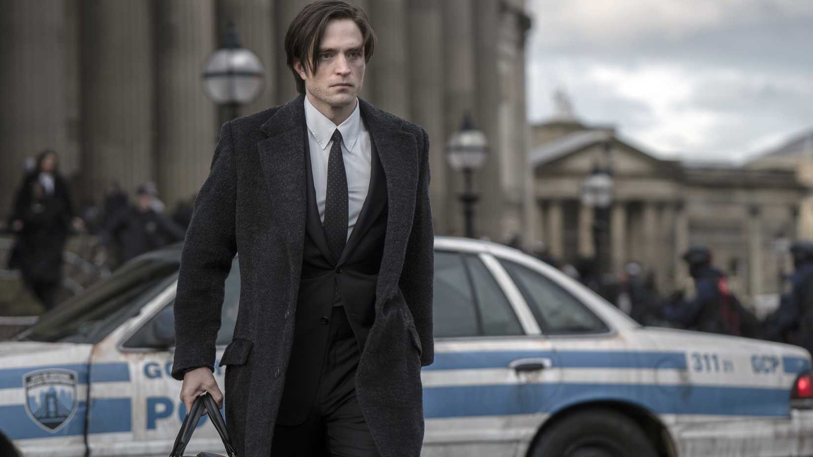Robert Pattinson as Bruce Wayne in The Batman walking in front of a police car