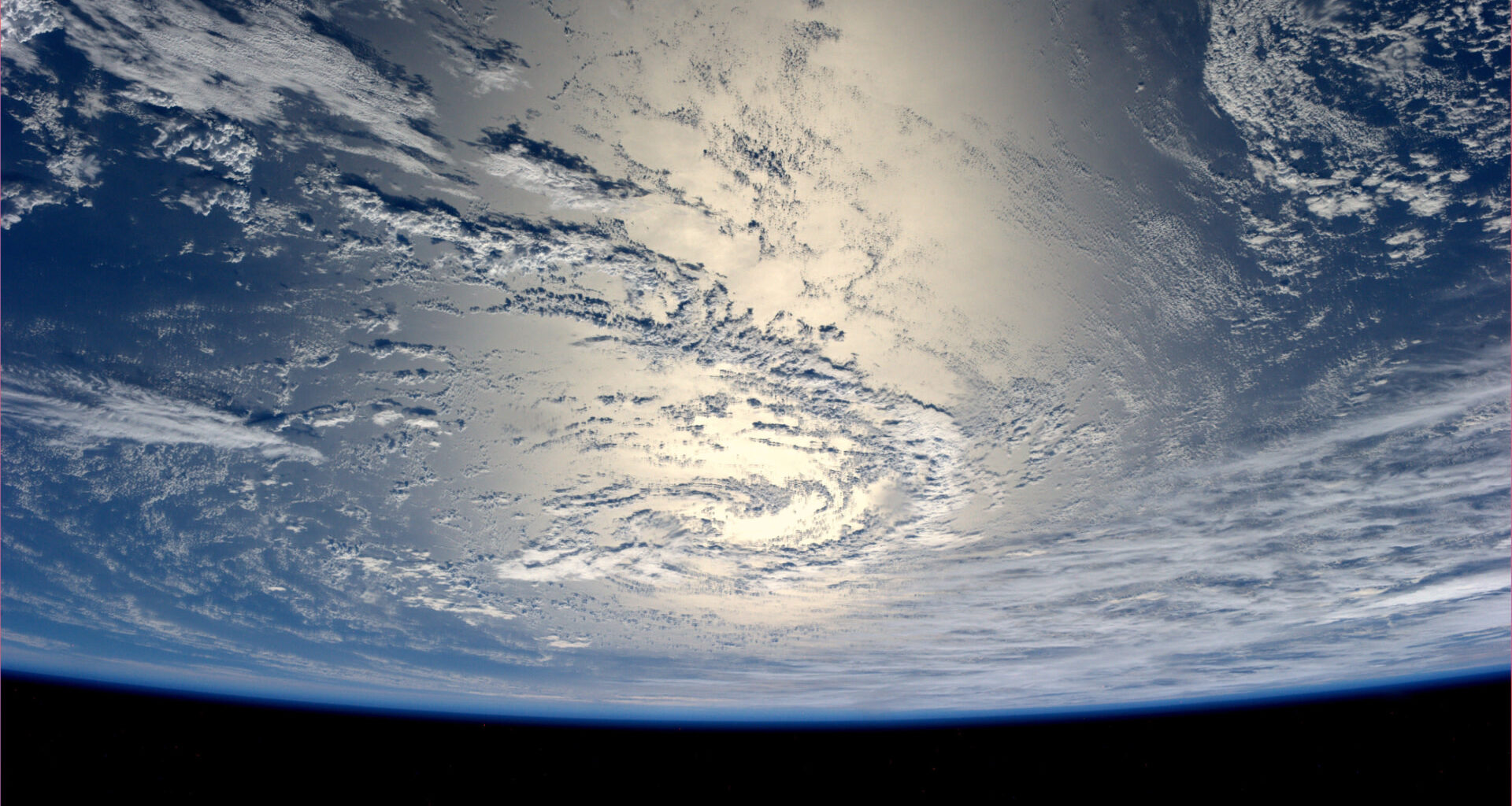 View of Earth from space, showing a vast expanse of clouds over the ocean with sunlight reflecting off the water.