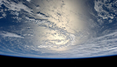 View of Earth from space, showing a vast expanse of clouds over the ocean with sunlight reflecting off the water.