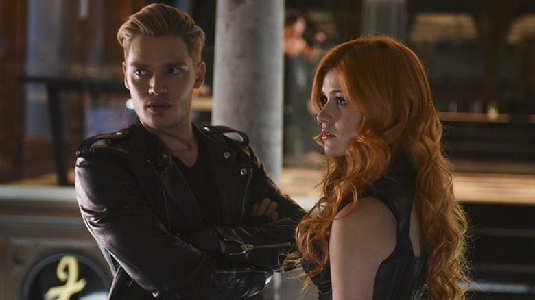 Jace in leather jacket standing next to Clary with red hair and leather top
