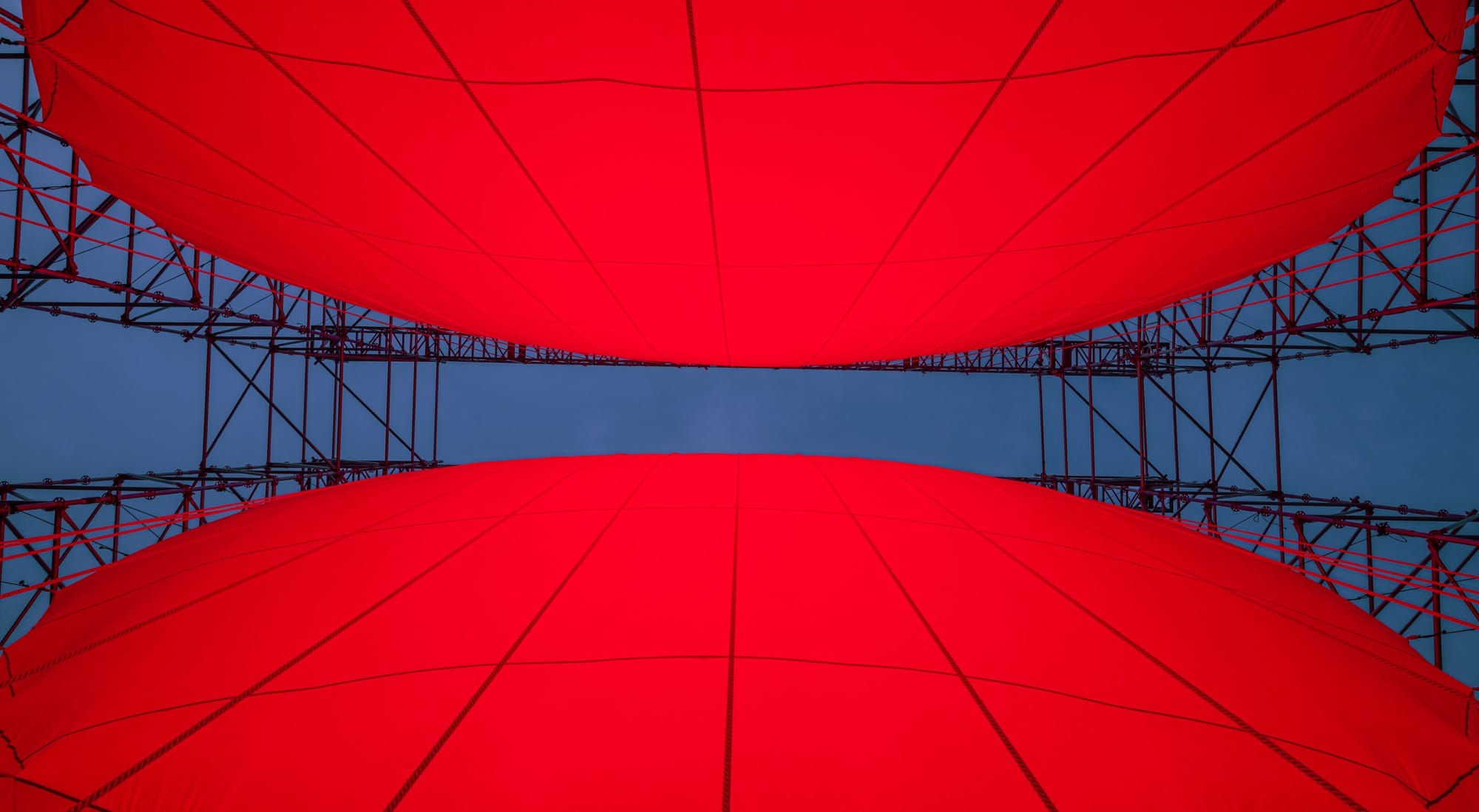 A detail, looking up from from inside, of a large-scale installation by SpY of two glowing, red half-spheres within a metal framework