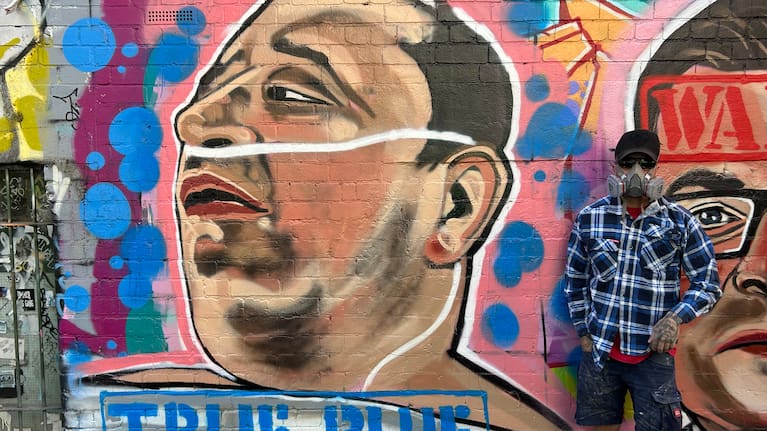 Street artist Jarrod Grech poses for a photo next to his painting of Ahmed al Ahmed.