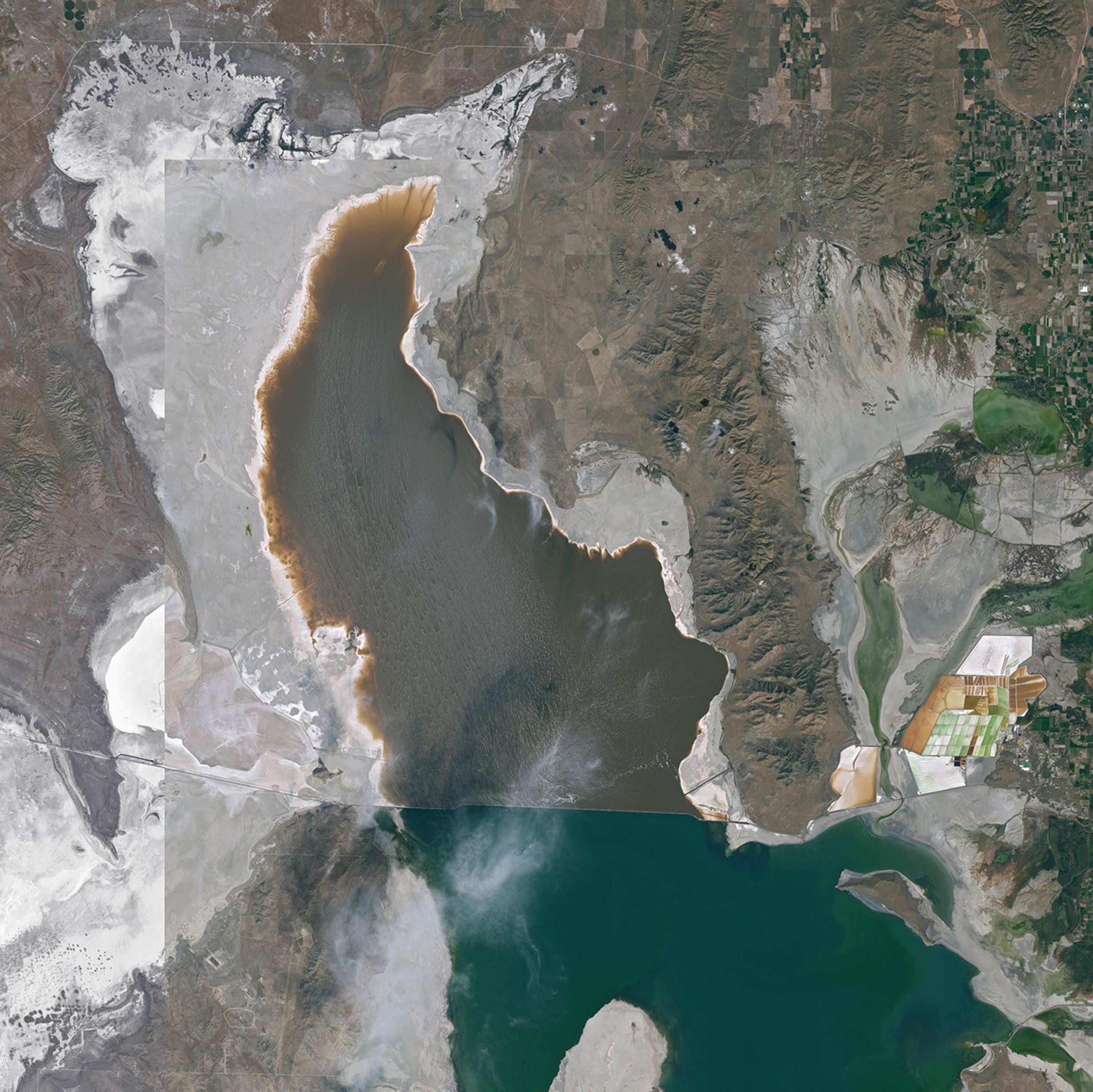 A satellite image of the Great Salt Lake shoreline in 2025 shows exposed gray lakebed with clusters of small dark mounds.