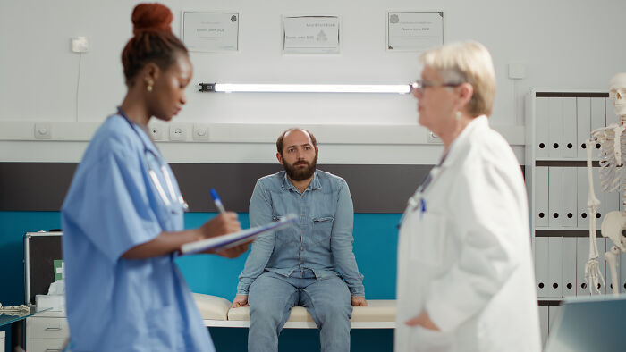 Patient sitting on hospital bed looking concerned while medical staff discuss leaving against medical advice.