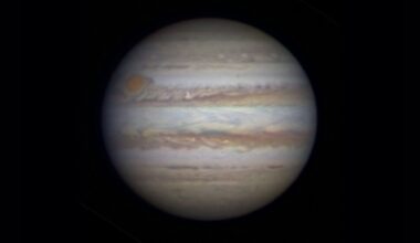 Photo of Jupiter as seen through a telescope. A large white sphere with swirling rings of red and brown around it against a black background.