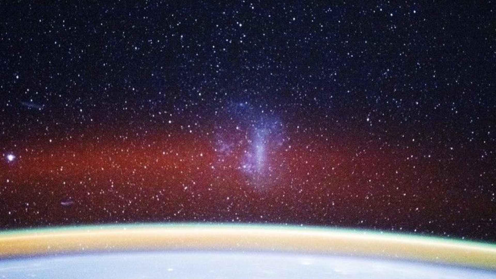 A curved white arc at the bottom of the image glows with a gold band and red fuzzy band of light above it with stars in the distance and a smoky purple shape in the center of the image