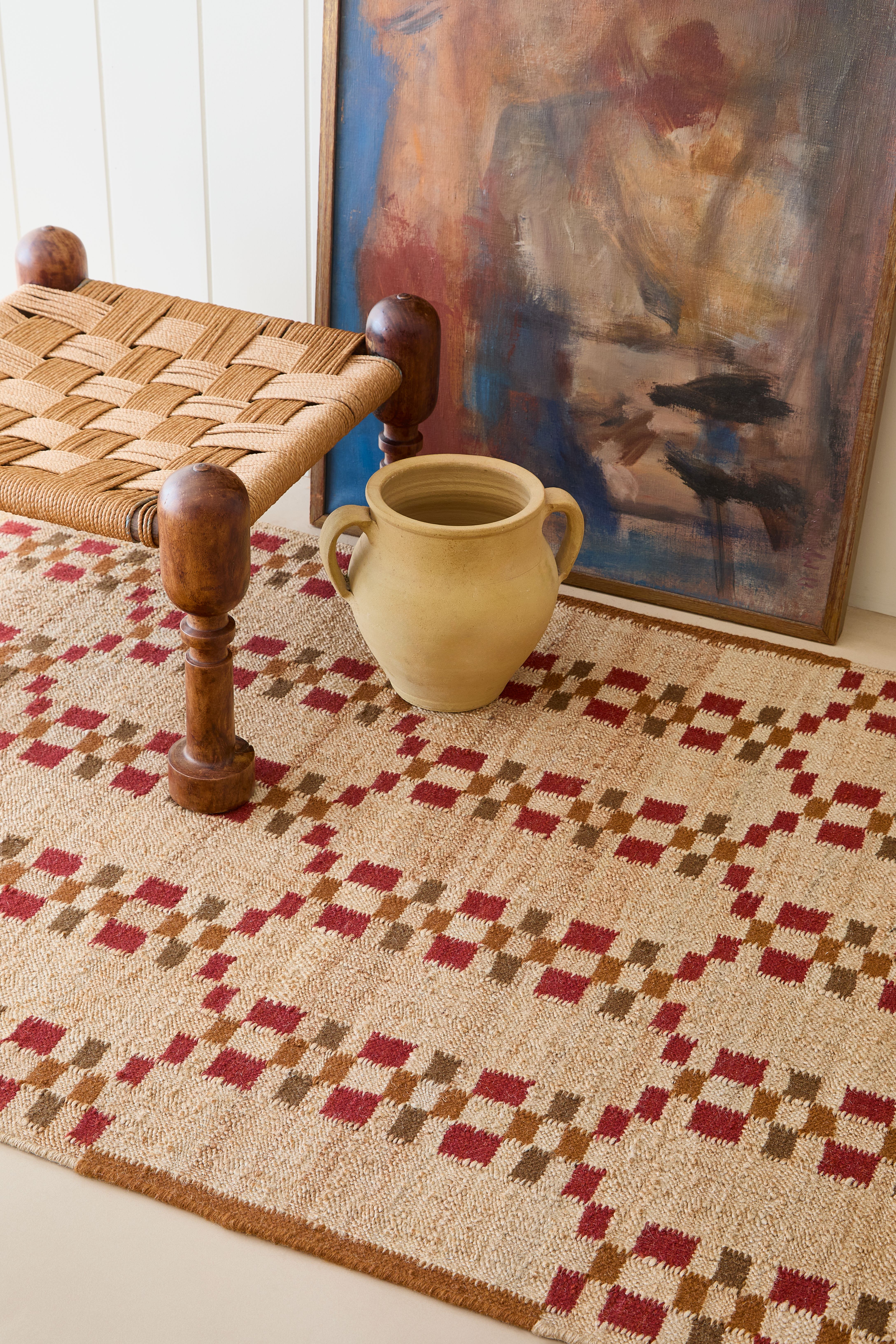 Jute flatweave rug in a geometric pattern of red and brown squares on a beige background.