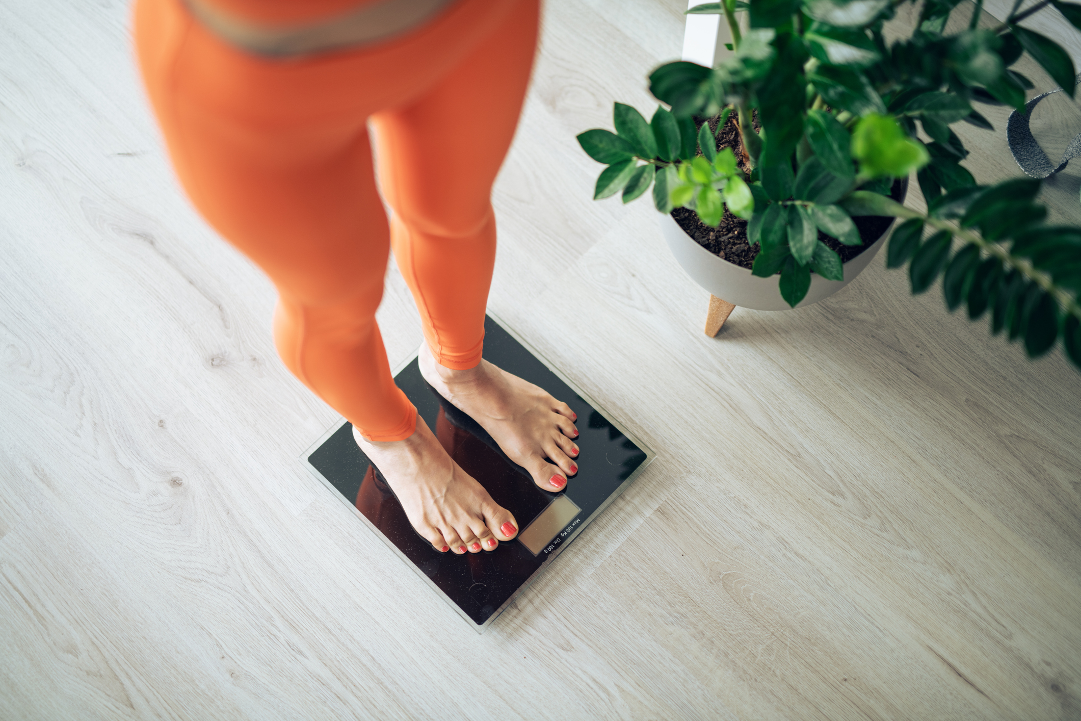 Woman in orange sport clothes measuring weight on a scale at home.