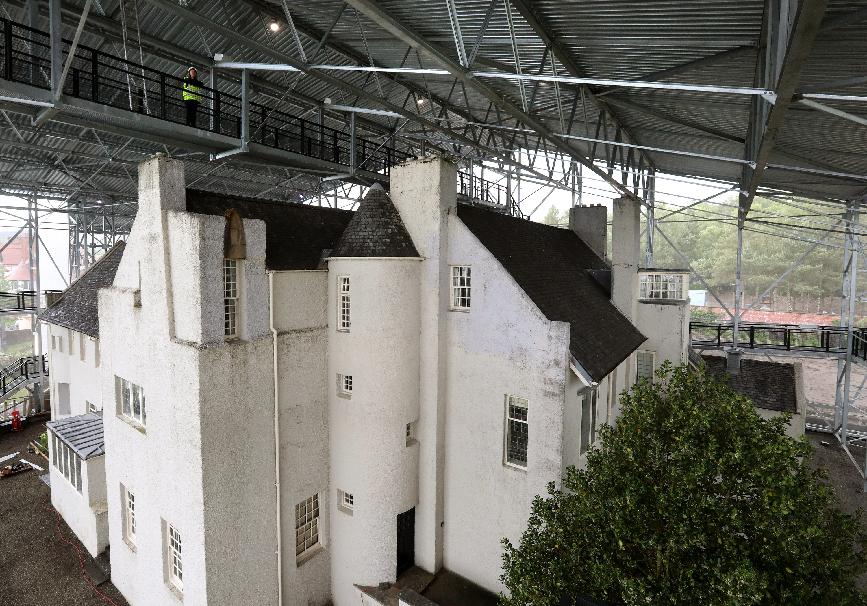 A visitor services assistant walks on a suspended walkway inside the 'Box' surrounding Charles Rennie Mackintosh's Hill House.
