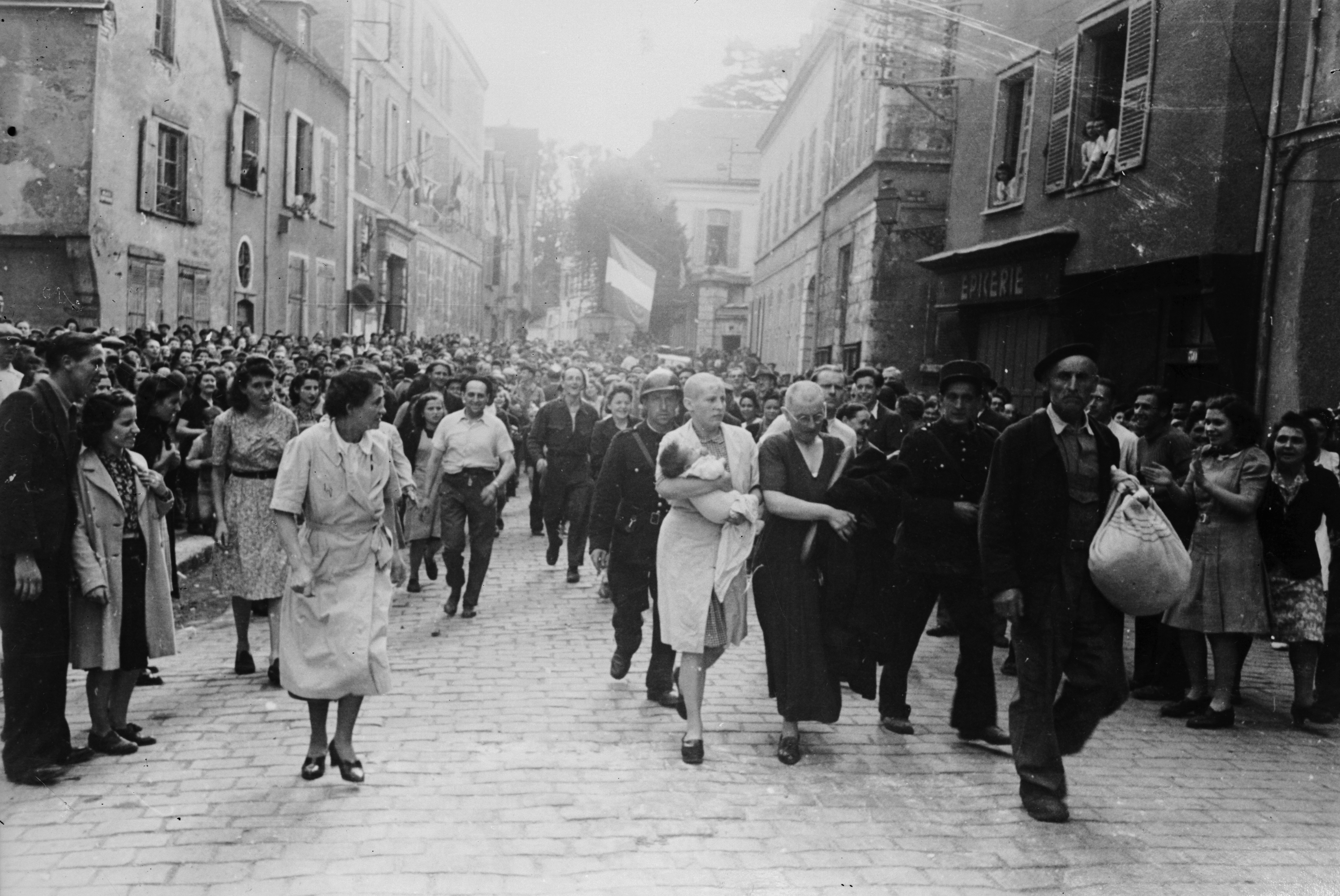 Shaved women and their children are marched through a crowd of jeering civilians in Chartres, France, as punishment for collaboration with German forces.
