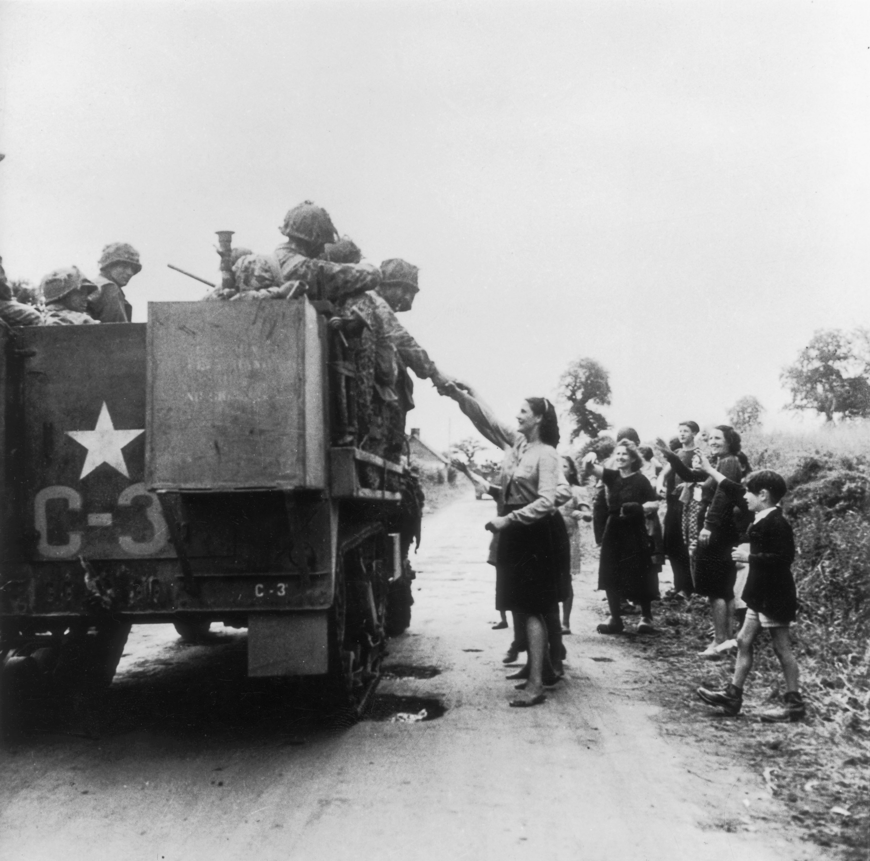 American troops in a military truck greeted by French civilians.