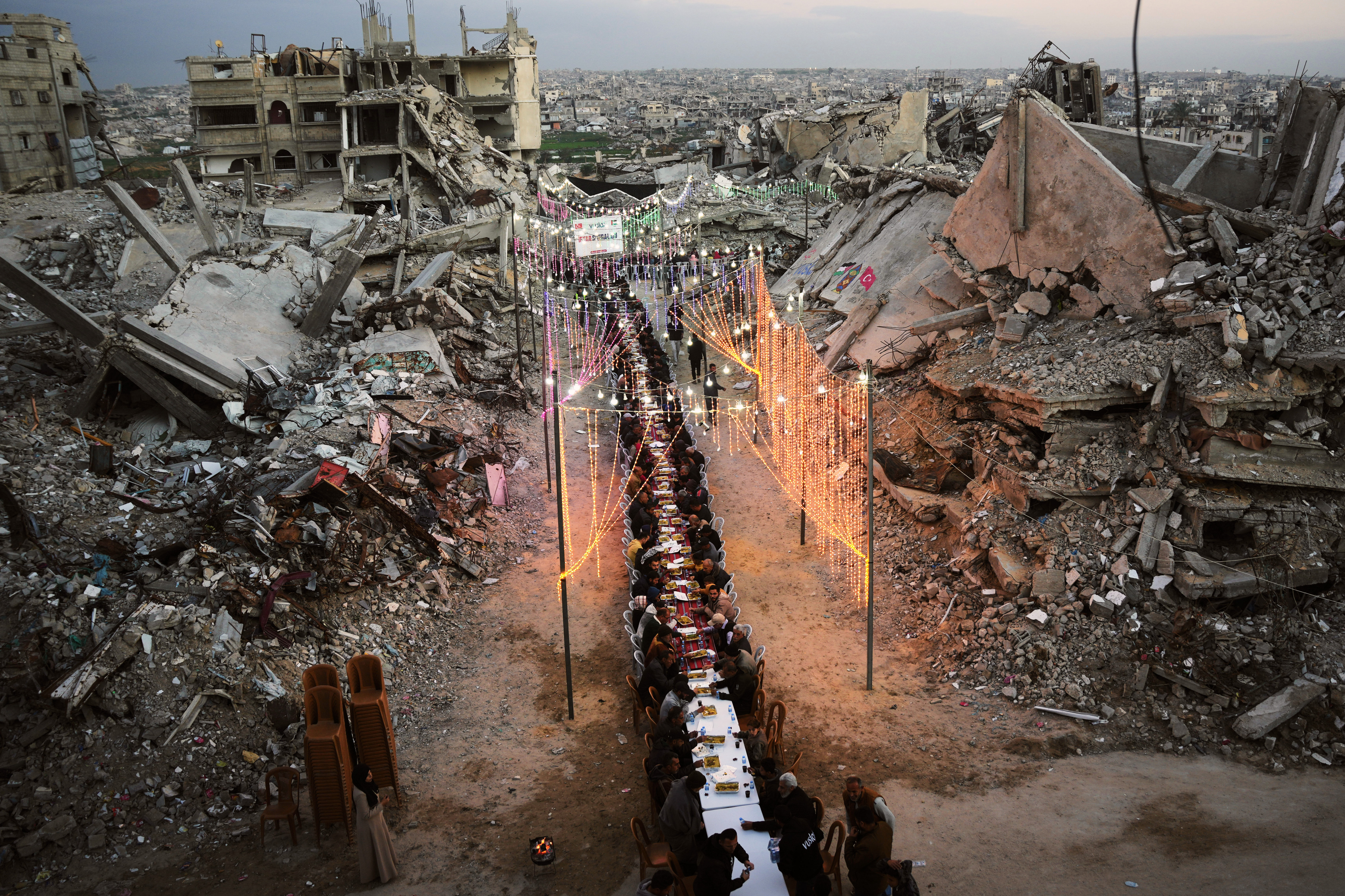 Palestinians gather for an iftar meal at a long table amidst destroyed buildings and rubble in Khan Younis, Gaza Strip.