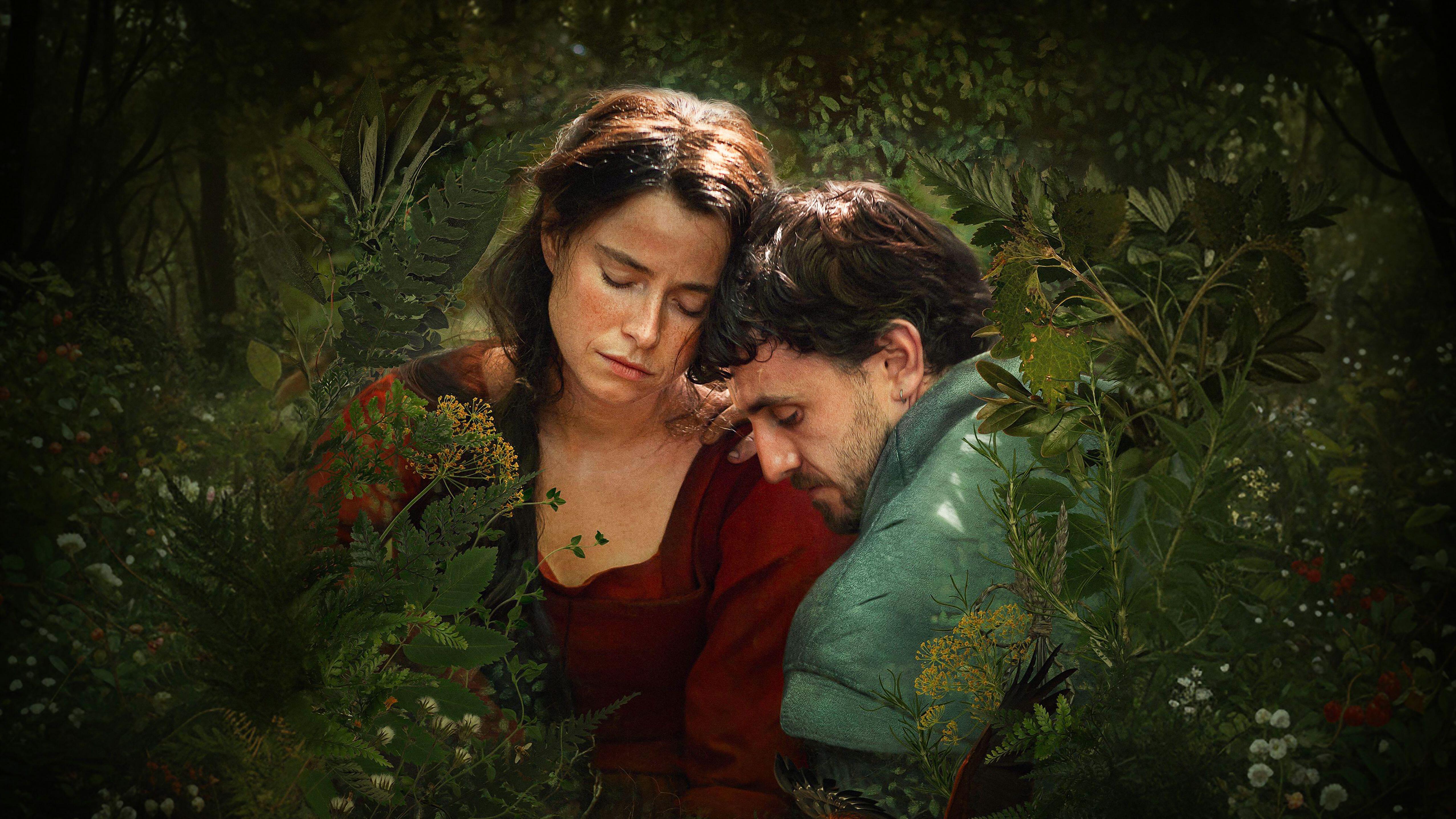 Jessie Buckley and Paul Mescal in character for the film "Hamnet," surrounded by lush greenery and flowers.