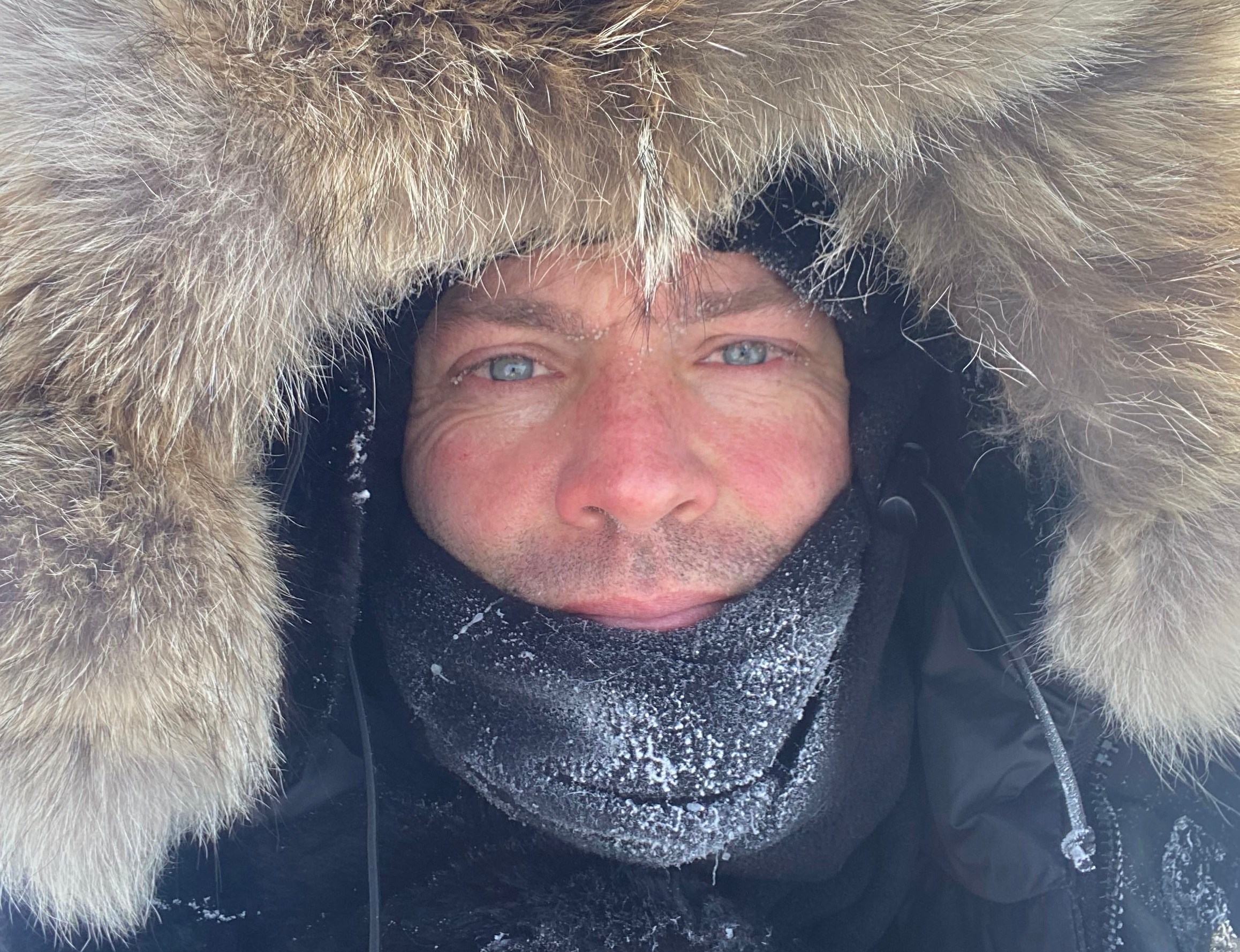 Man wearing a fur-lined hood and a frost-covered face covering.