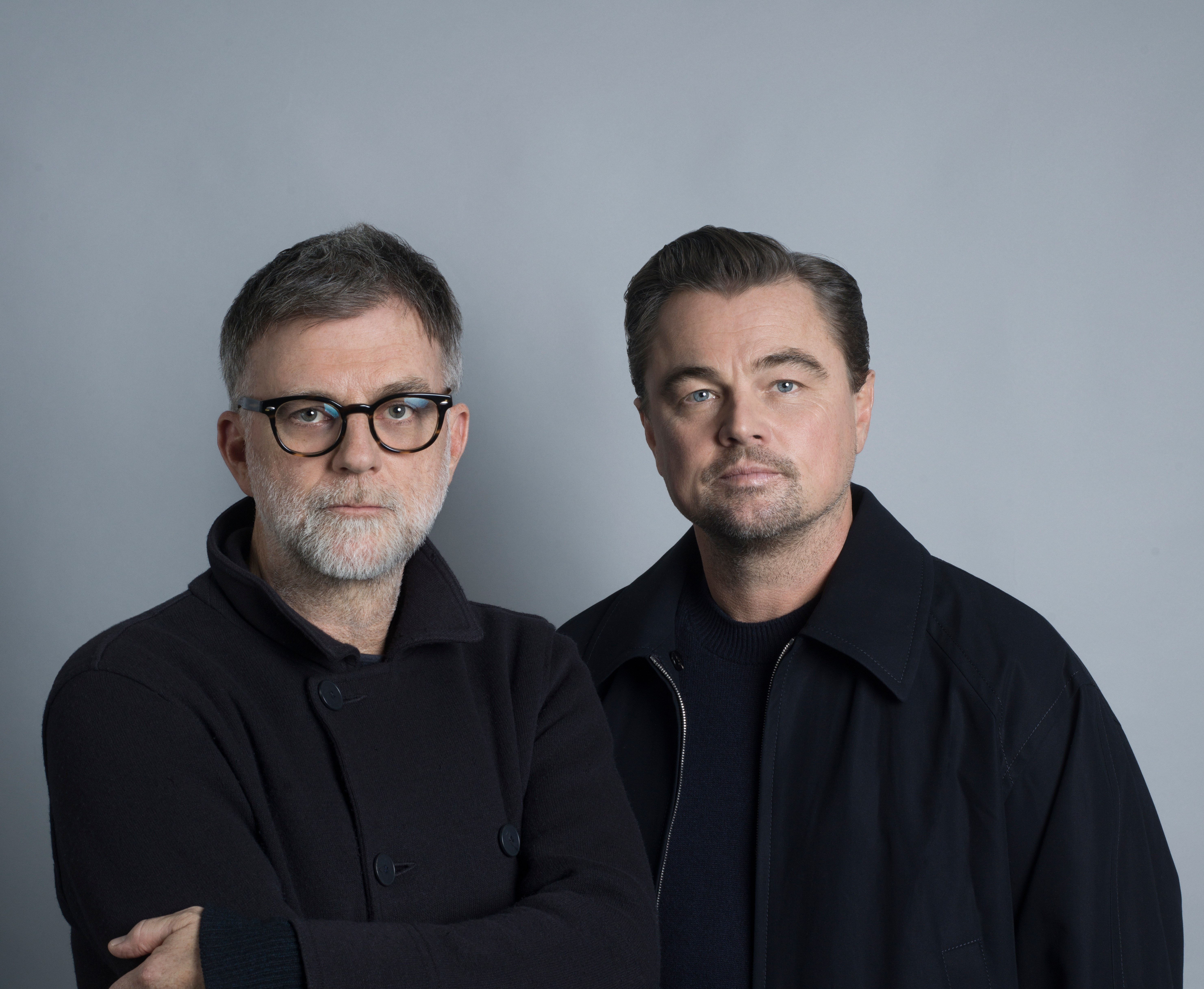 Leonardo DiCaprio and Paul Thomas Anderson in dark clothing against a gray background.