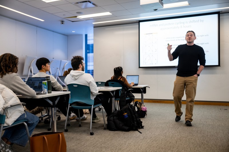 Schlichting stands in front of a whiteboard and powerpoint, students sitting at their desks.