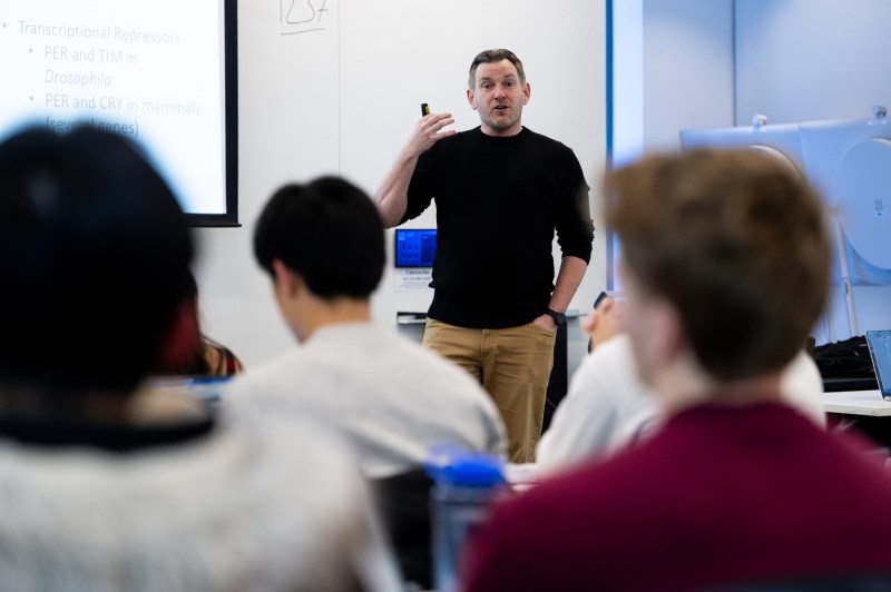 Schlichting describes a biological concept in class, gesturing with a powerpoint controller.