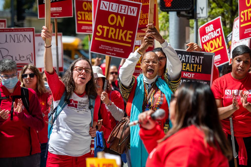 Hundreds of protestors in red T-shirts hold red and yellow picket signs outside of UCSF Benioff Children's Hospital Oakland.
