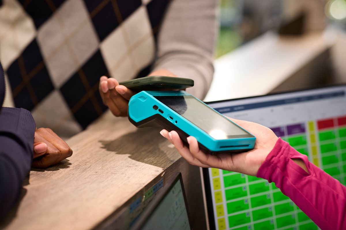 Male customer using smart phone while making payment through credit card reader at golf shop