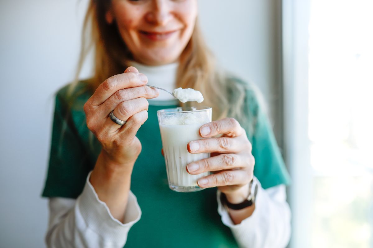 mature woman with long hair eats fresh homemade yogurt from a glass near the window, a healthy joyful morning and sincere emotions.