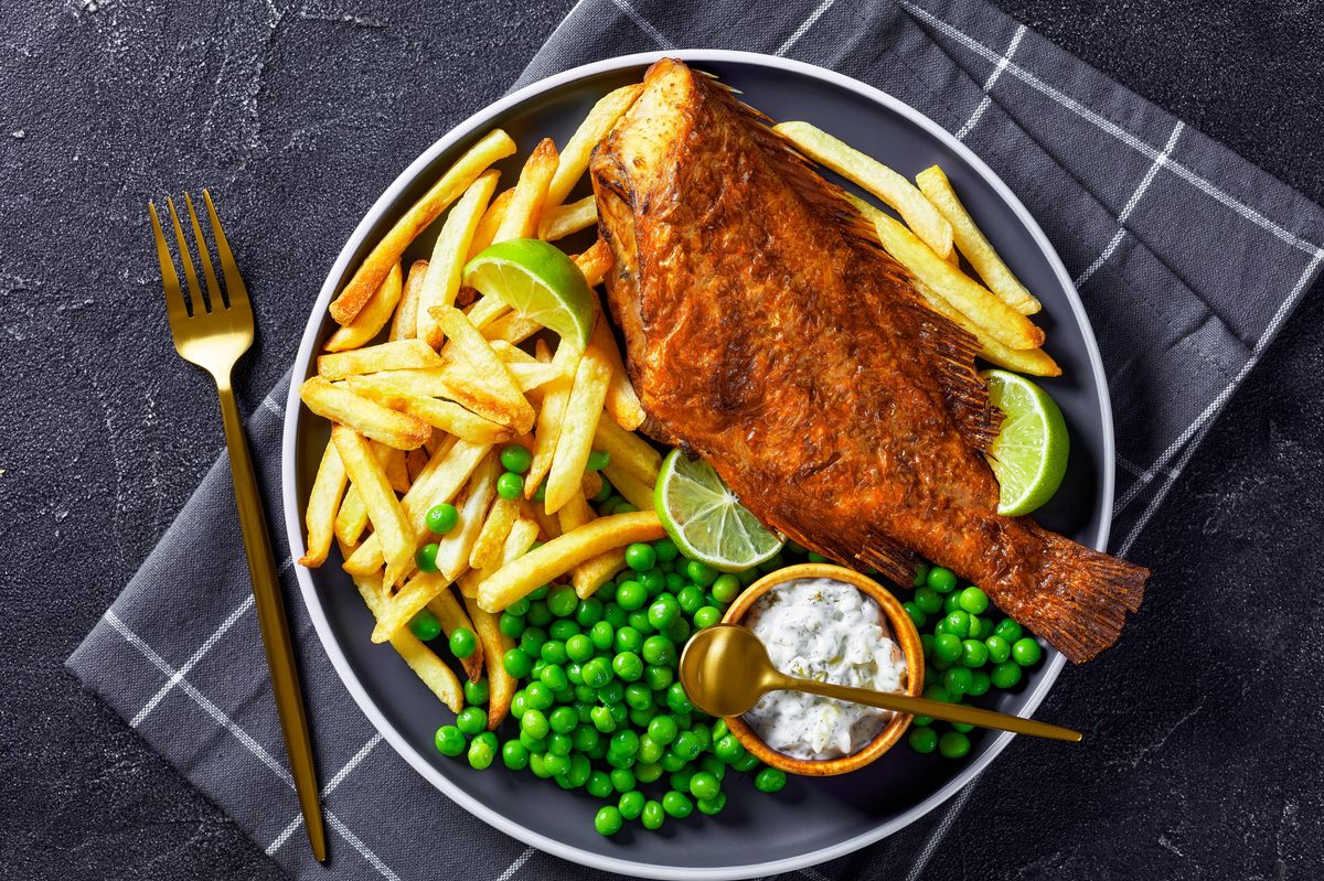 fried Atlantic redfish on a plate with french fries, boiled green peas, tartar sauce and lime slices, horizontal view from above, flat lay, close-up
