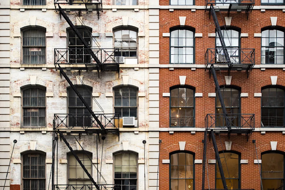 Exterior view of a classic urban building with brick and stone facade, featuring fire escapes on multiple floors