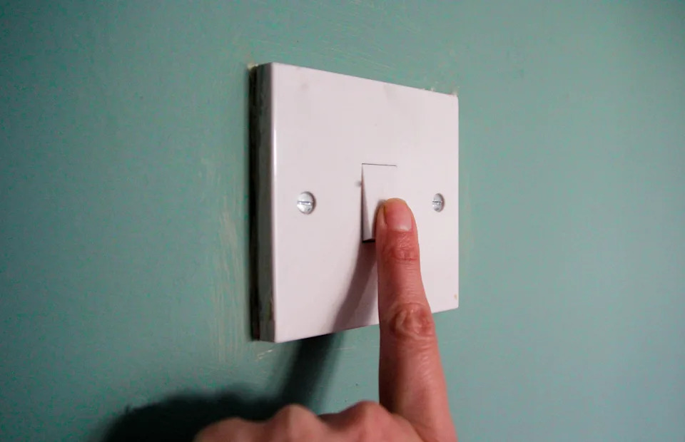 Finger pressing a light switch on a wall, symbolizing energy conservation or budget-friendly home practices