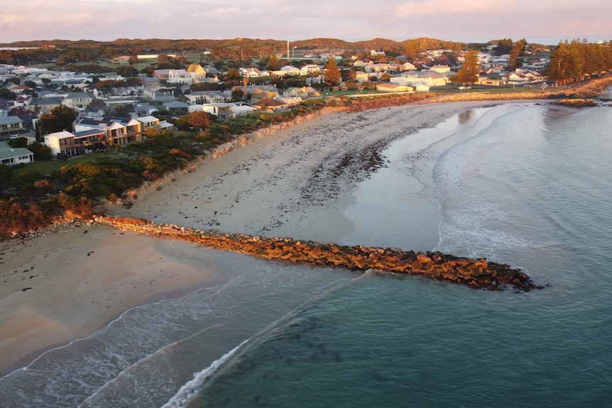 A beach at sunrise, with a groyne, and houses behind the dunes