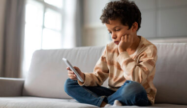 an elementary school student sits on a sofa looking at a smartphone