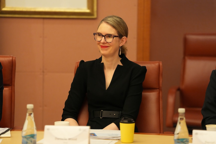 Danielle Wood smiles and wears glasses sitting at a table.
