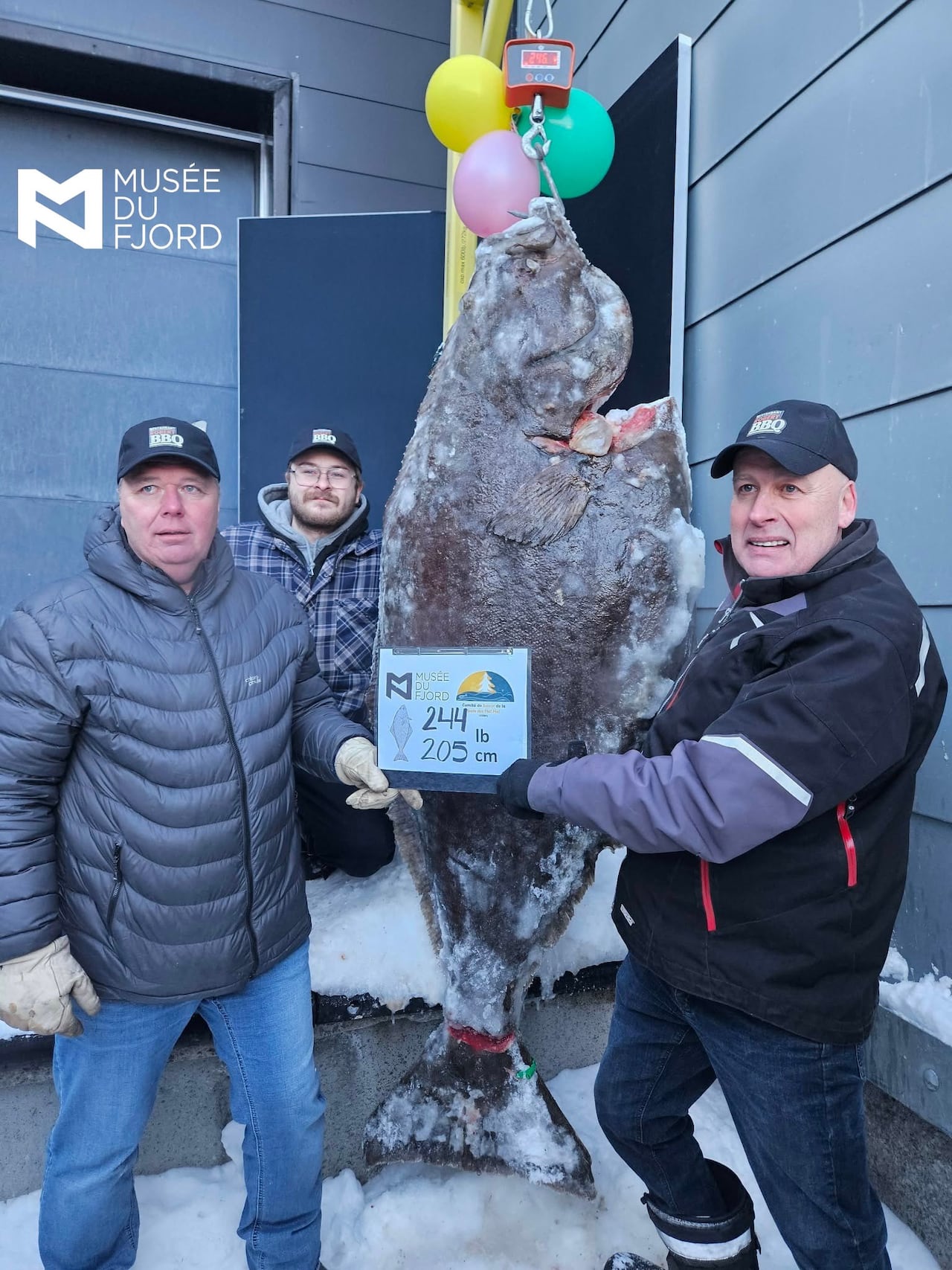 Three men stand next to a fish