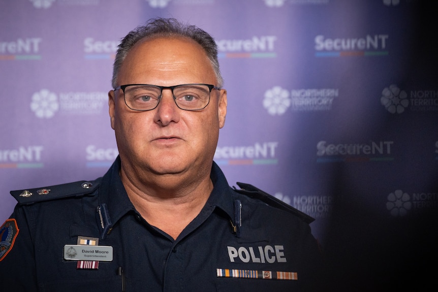 A man standing in front of a banner inside a room and speaking to someone off-camera.
