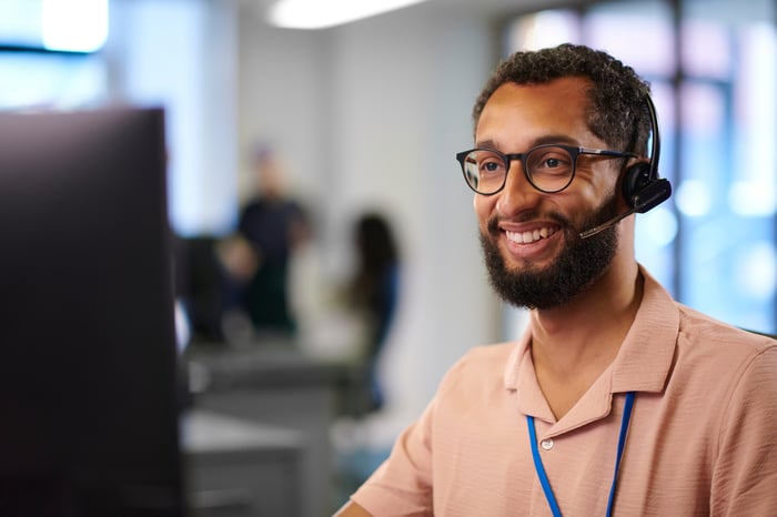 A person wearing a phone headset looking at a computer monitor.