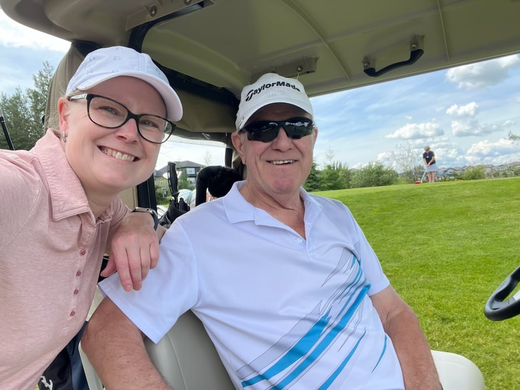 A woman in a pink shirt and a man sitting in a golf cart.