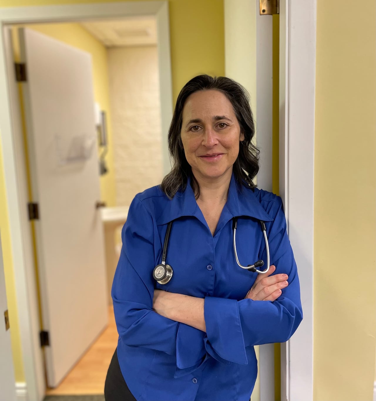 A physician in a blue shirt stands in her office. 
