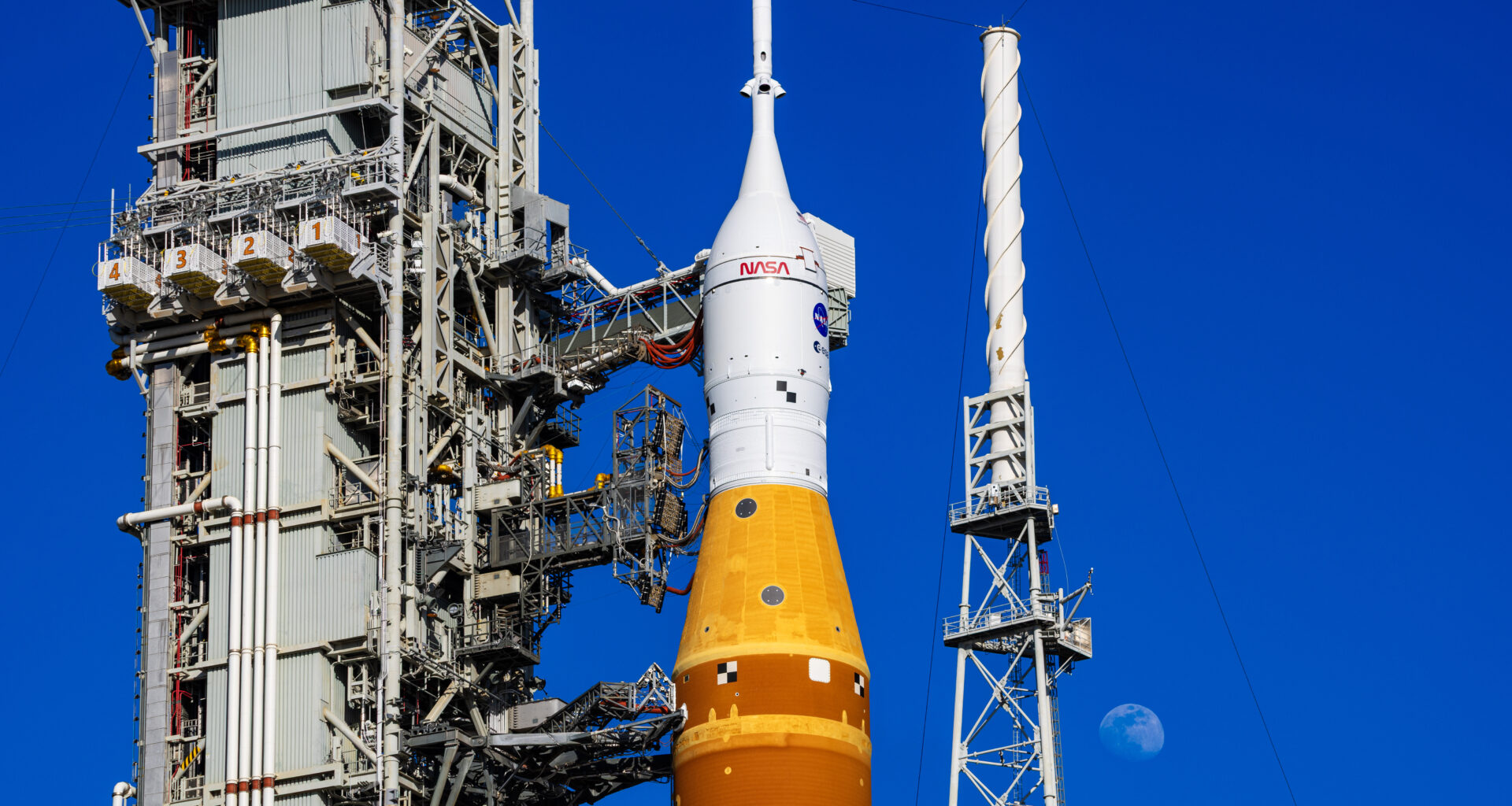 The Moon is seen behind the SLS (Space Launch System) and Orion spacecraft, atop the mobile launcher on January 28, 2026. The rocket is currently at Launch Pad 39B at NASA’s Kennedy Space Center in Florida, as teams are preparing for a wet dress rehearsal to practice timelines and procedures for the launch of Artemis II. 508 Description:The Moon is seen shining over the SLS (Space Launch System) and Orion spacecraft, atop the mobile launcher on January 29, 2026. The rocket is currently at Launch Pad 39B at NASA’s Kennedy Space Center in Florida, as teams are preparing for a wet dress rehearsal to practice timelines and procedures for the launch of Artemis II.