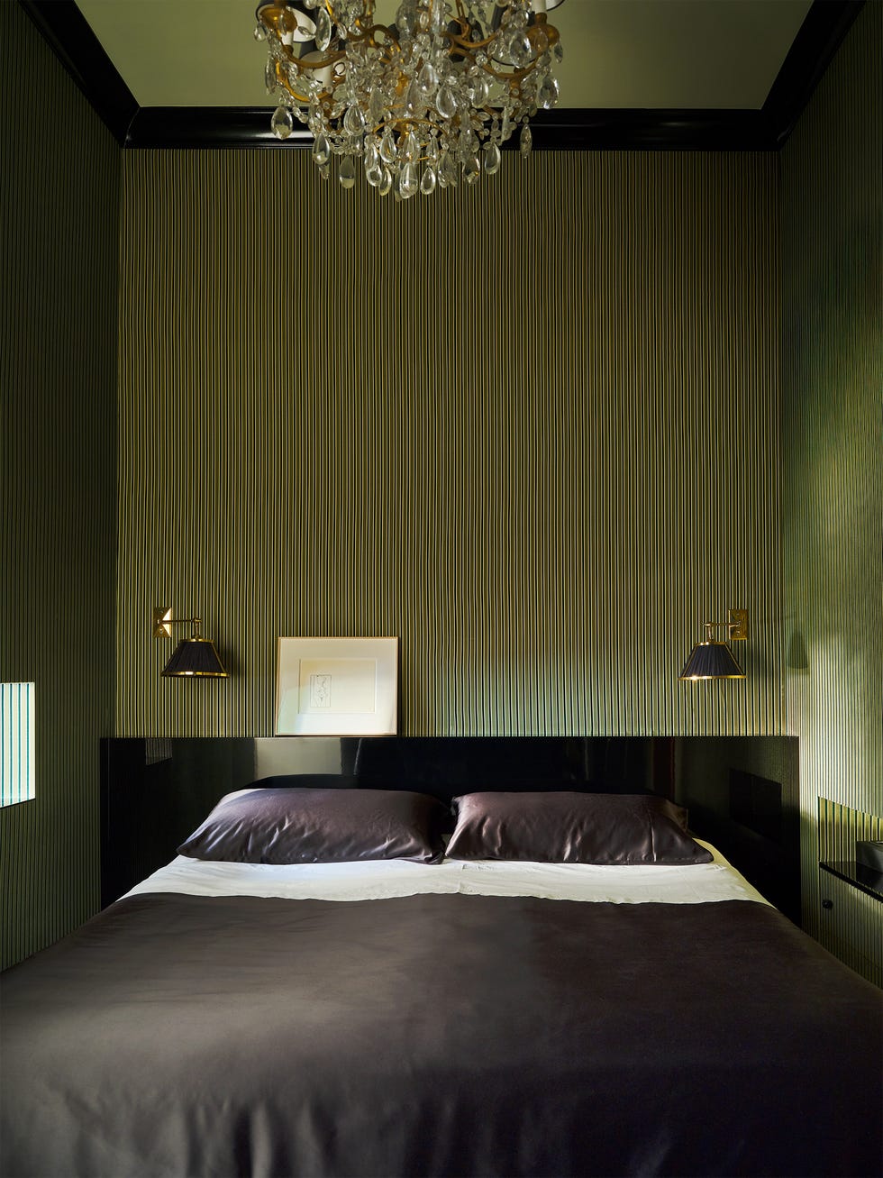 Cozy bedroom featuring a bed, patterned wall, and chandelier.