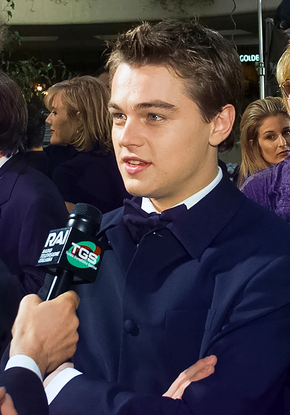 A person in a formal suit is being interviewed on the red carpet, surrounded by other attendees