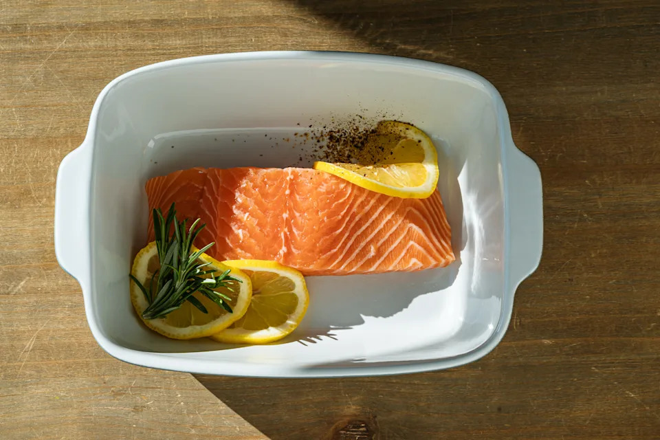 Fresh salmon fillet with lemon slices and rosemary in dish, preparing food, ingredients, close up. directly above. Sunlight with harsh shadows