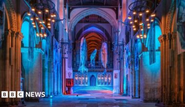 Three models of sperm whales hang in the nave of Winchester Cathedral, which has been lit in blue to recreate the ocean.