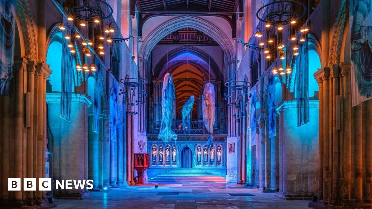 Three models of sperm whales hang in the nave of Winchester Cathedral, which has been lit in blue to recreate the ocean.