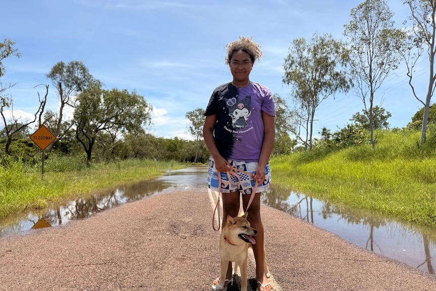 A young girl smiling, with a dog in hand in front of flooded road