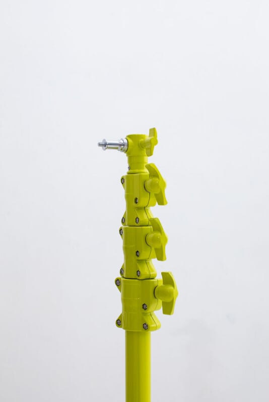 A bright yellow adjustable stand with three tightening knobs and a silver screw mount on top, standing against a plain white background.