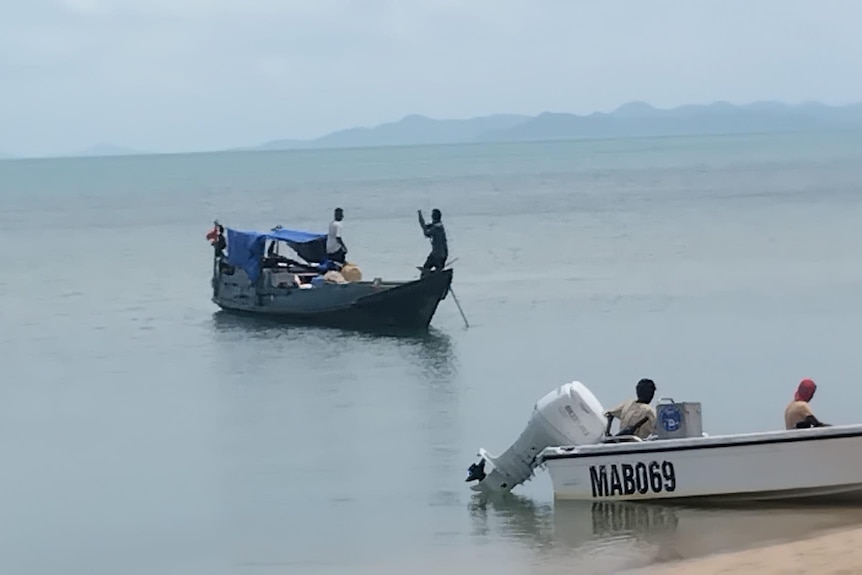several small fishing boats and people on a tropical island beach.